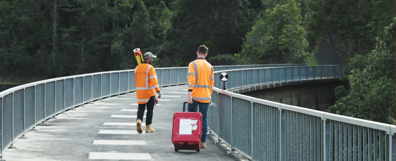 Image of two people crossing a bridge with surveying equipment